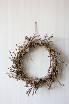 a wreath of willow twigs with fluffy buds made with your own hands hangs on a white wall, vertical frame