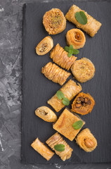 traditional arabic sweets (kunafa, baklava) on a black slate board on a black concrete background.top view, close up.