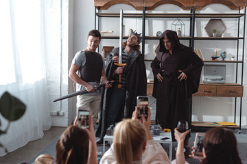 back view of girls taking photo of young men in fairy costumes on smartphones