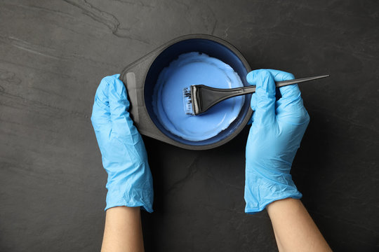 Woman preparing dye for hair coloring at black stone table, top view