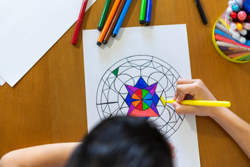 High angle shot of a boy painting a mandala with his colored markers