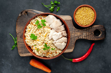Bulgur with vegetables and chicken fillet on a stone background.