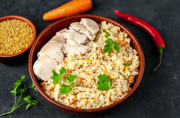Bulgur with vegetables and chicken fillet on a stone background.