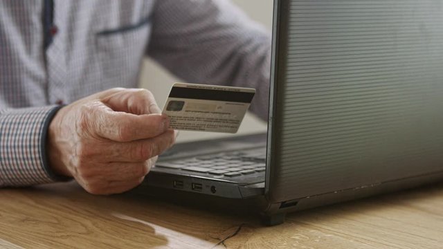 Senior man paying on the online shop using the credit card. Close up shot on the wrinkled hand