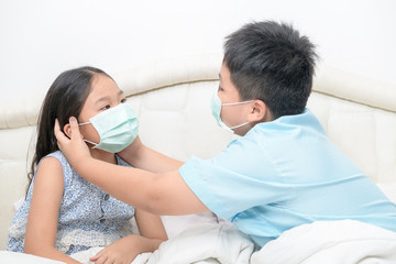 Brother helping his sister wearing surgical mask on bed,