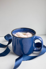 coffee with marshmallow and milk in a massive blue cup on a white background with ribbons and...