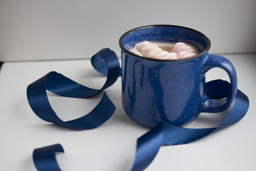 coffee with marshmallow and milk in a massive blue cup on a white background with ribbons and...