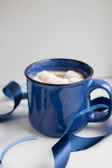 coffee with marshmallow and milk in a massive blue cup on a white background with ribbons and...