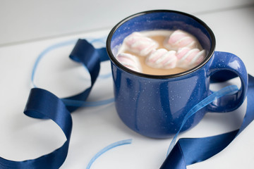 coffee with marshmallow and milk in a massive blue cup on a white background with ribbons and...