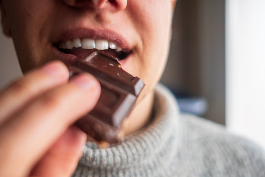 a person enjoying a piece of chocolate with hazelnuts. Eating chocolate and holding it with her hand.