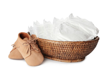 Wicker bowl with disposable diapers and child's shoes on white background