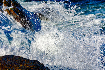 Fototapeta premium Detail of wave breaking over stones with foam, water drops and splash