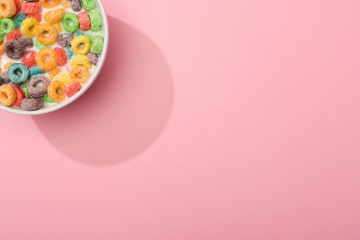 top view of bright colorful breakfast cereal with milk in bowl on pink background