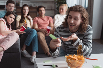 selective focus of smiling man holding sticky note while playing name game with friends