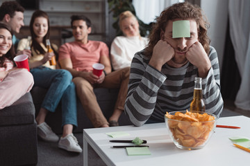 selective focus of bored man with sticky note on forehead playing name game with friends