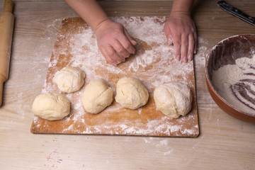 A woman kneads the dough. Plywood cutting board, wooden flour sieve and wooden rolling pin - tools for making dough.