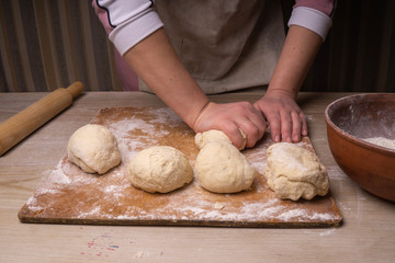 A woman kneads the dough. Plywood cutting board, wooden flour sieve and wooden rolling pin - tools for making dough.