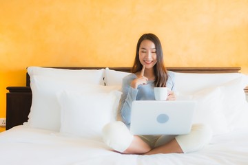 Portrait beautiful young asian woman using computer notebook or laptop with coffee cup on bed