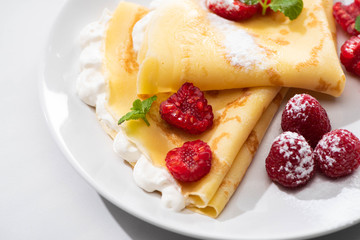 close up view of tasty crepes with raspberries and whipped cream on plate