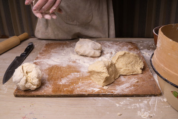 A woman kneads the dough. Plywood cutting board, wooden flour sieve and wooden rolling pin - tools for making dough.