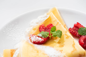 close up view of tasty crepes with raspberries and whipped cream on plate
