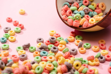Fototapeta na wymiar selective focus of bright colorful breakfast cereal scattered from bowl on pink background