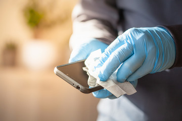man hands in gloves disinfecting smartphone, eliminating germs coronavirus bacteria