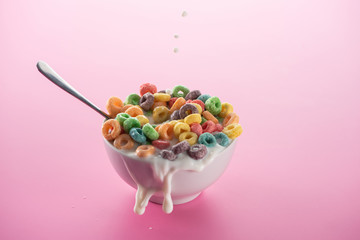 bright multicolored breakfast cereal in bowl with splashing milk and spoon on pink background