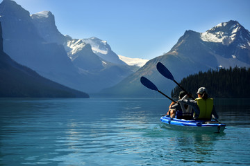 Two people in a double kayak on an aqua green lake in the Canadian rocky mountains