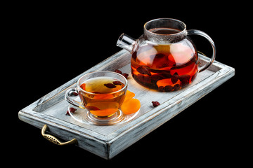 Hot tea with rose hips and dried apricots in a glass teapot. On dark background