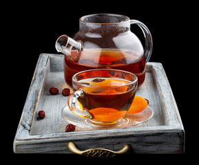 Hot tea with rose hips and dried apricots in a glass teapot. On dark background