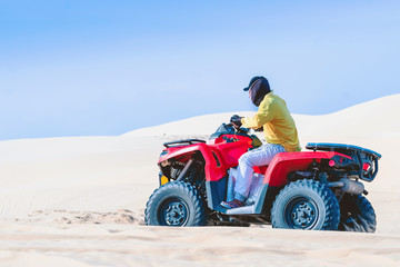 Tourist enjoy riding the quad bike or powerful fast off-road four-wheel drive ATVs at white sand dunes in Mui Ne, Vietnam.