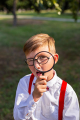 vertical portrait of a cheerful inquisitive schoolboy against a green park
