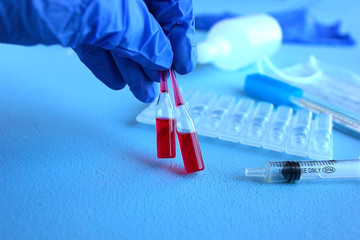 A hand in a blue medical glove holds ampoules with red liquid, next to a syringe, medicine, chlorhexidine, antispetic and thermometer.