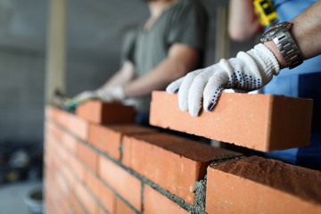 Two workers making red brick wall at construction site
