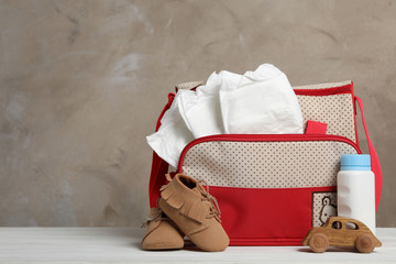 Bag with diapers and baby accessories on white wooden table. Space for text