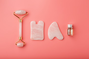 Obraz na płótnie Canvas A set of tools for face Massage technique Gua Sha made of natural rose quartz on a pink background. Roller, jade stone and oil in a glass jar for face and body care.
