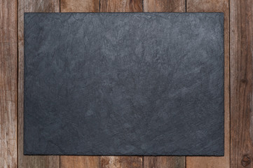 A serving black board made of stone lies on an old wooden background. copyspace