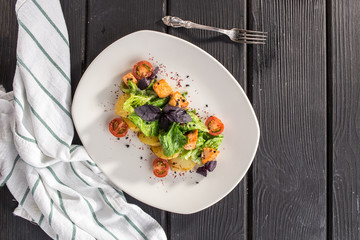 Smoked salmon and young potato warm salad with basil and tomato on black wooden table