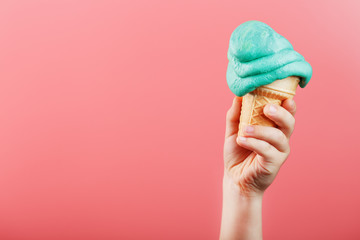 Ice cream in a child's hand melts on a pink background. The waffle cone with blue ice cream melts.