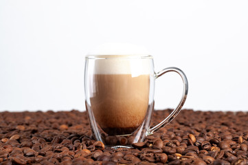  A transparent double-bottom latte cup stands among coffee beans on a white background. Copyspace