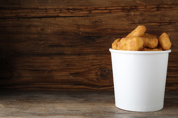 Bucket with tasty chicken nuggets on wooden table. Space for text