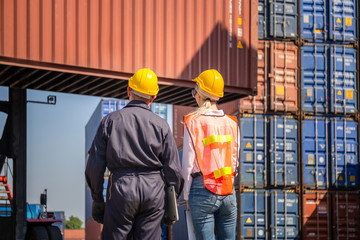 Worker man in hardhat and safety vest holding laptop and Female engineer control loading containers...