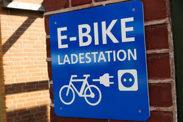 Obraz premium Isolated blue and white sign on brick wall with information for e-bike charging station (german word: Ladestation) - Germany
