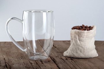  an empty transparent mug with a double bottom stands on an old wooden background, next to which coffee beans against a white background. copyspace