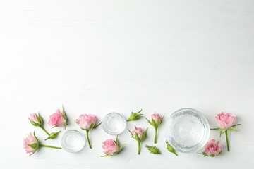 Flat lay composition with cosmetic gel and beautiful flowers on white wooden table. Space for text