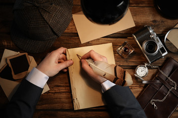Detective writing with feather on paper at wooden table, top view