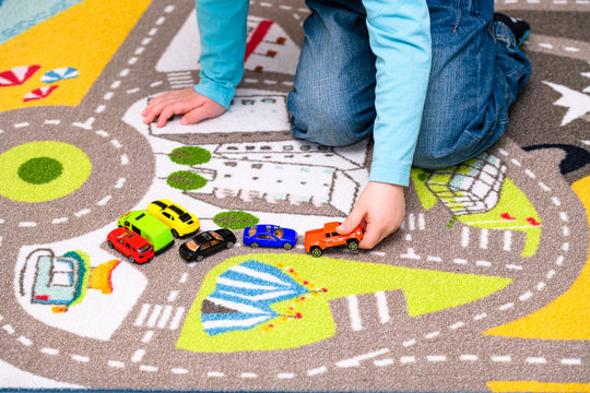 Five year old boy playing and lining up toy cars on a playing mat with roads. The cars have vivid colors and the boy is dressed in blue jeans and a blue shirt. He is holding a red toy truck.