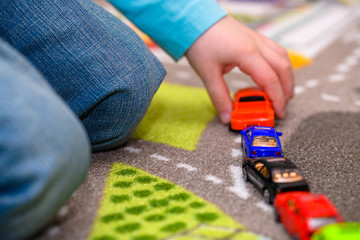 Close-up of five year old boy playing and lining up toy cars on a playing mat with roads. The cars...