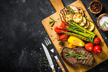 Beef steak grilled with vegetables on black stone table.